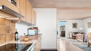 Een moderne keuken met houten kastjes, een inbouwoven en een aanrecht met een fles en glazen.