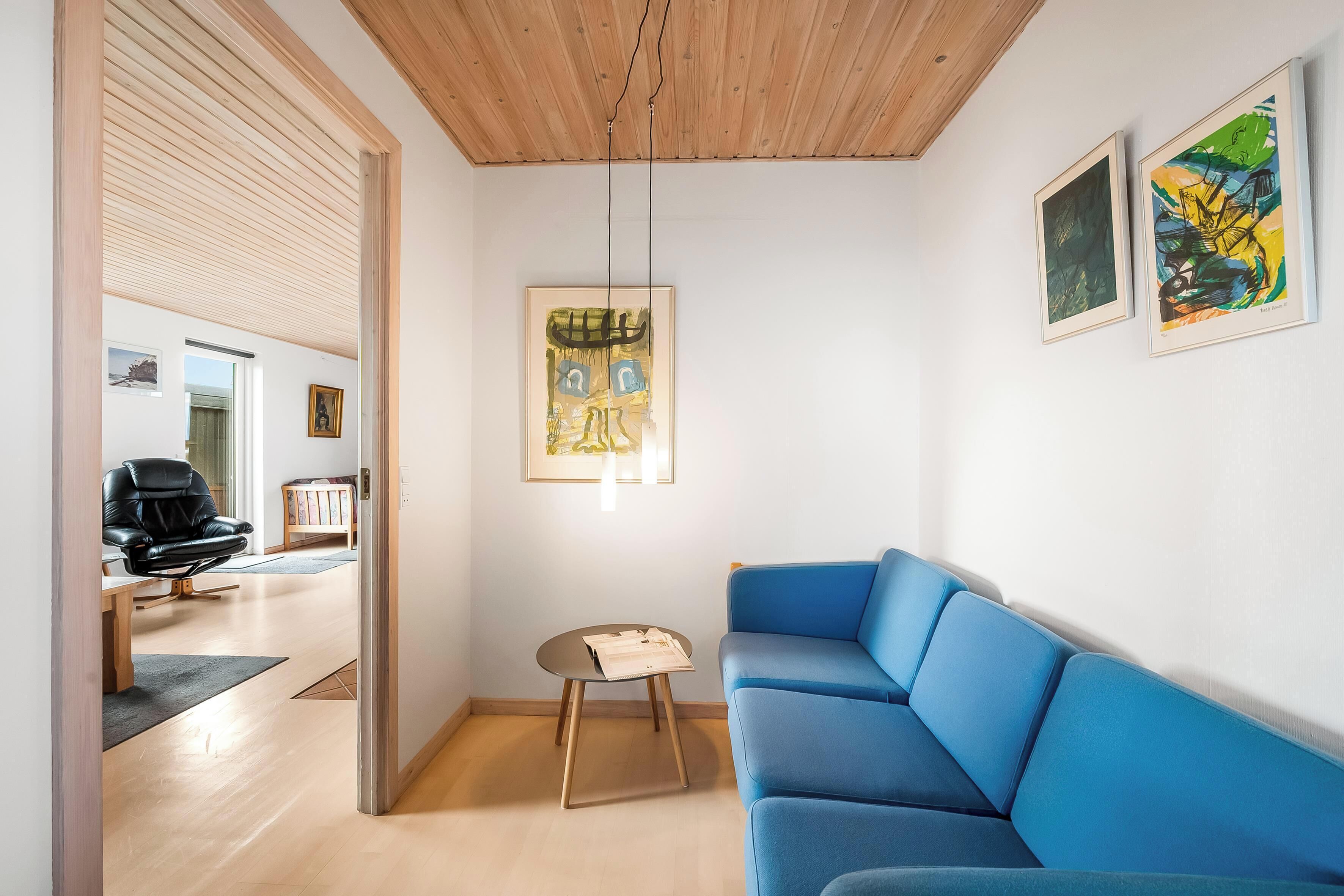 Una sala de estar moderna con un sofá azul, suelo de madera y obras de arte en las paredes.