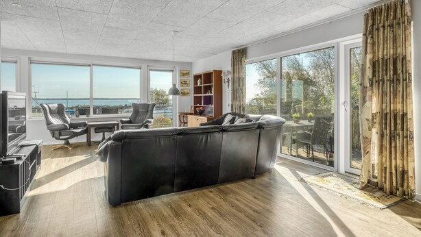 A modern living room with a black leather sofa, a wooden coffee table, and a large window offering a view of the outdoors.