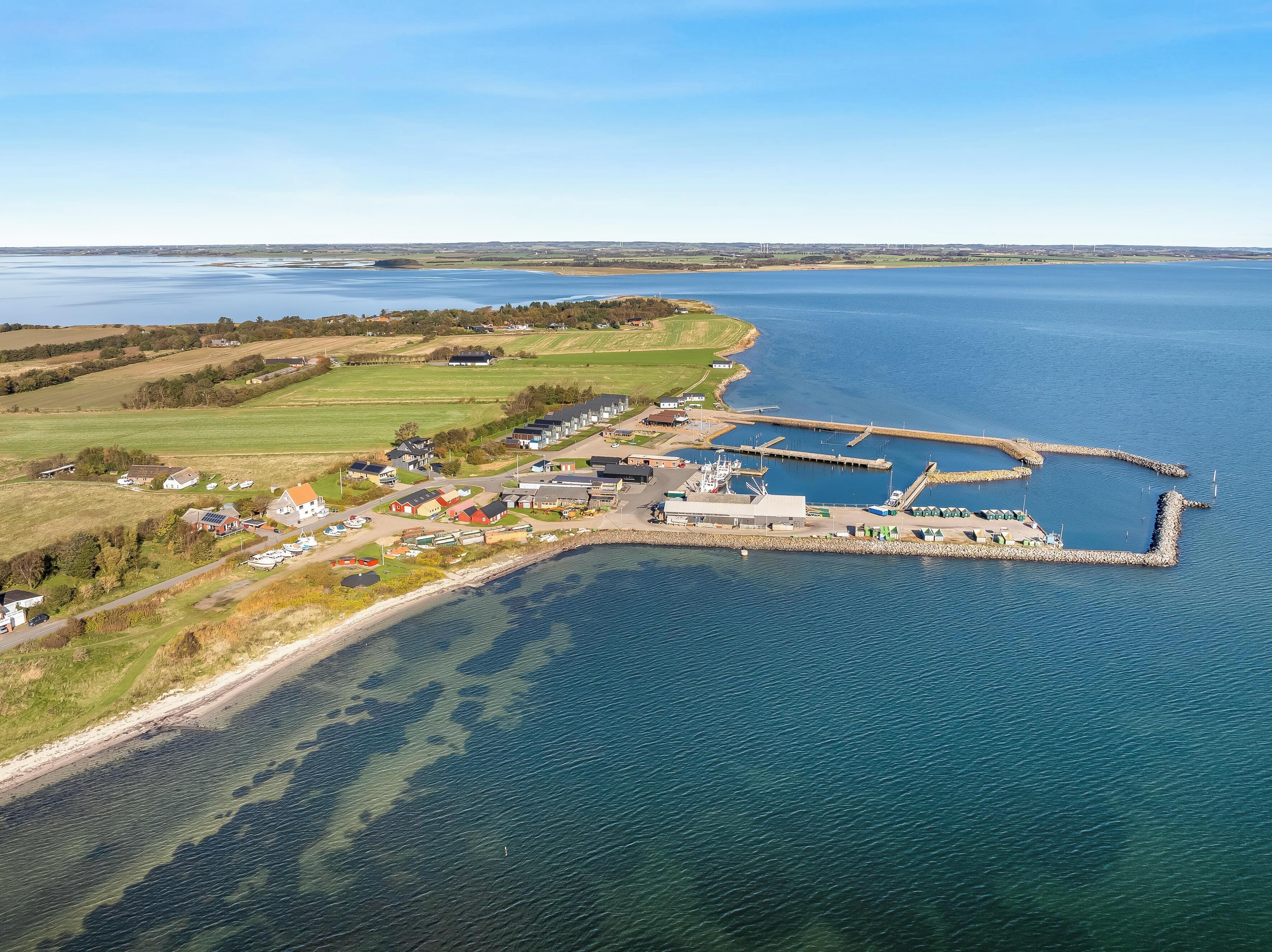 An aerial view of a coastal area with a marina, houses, and open fields.