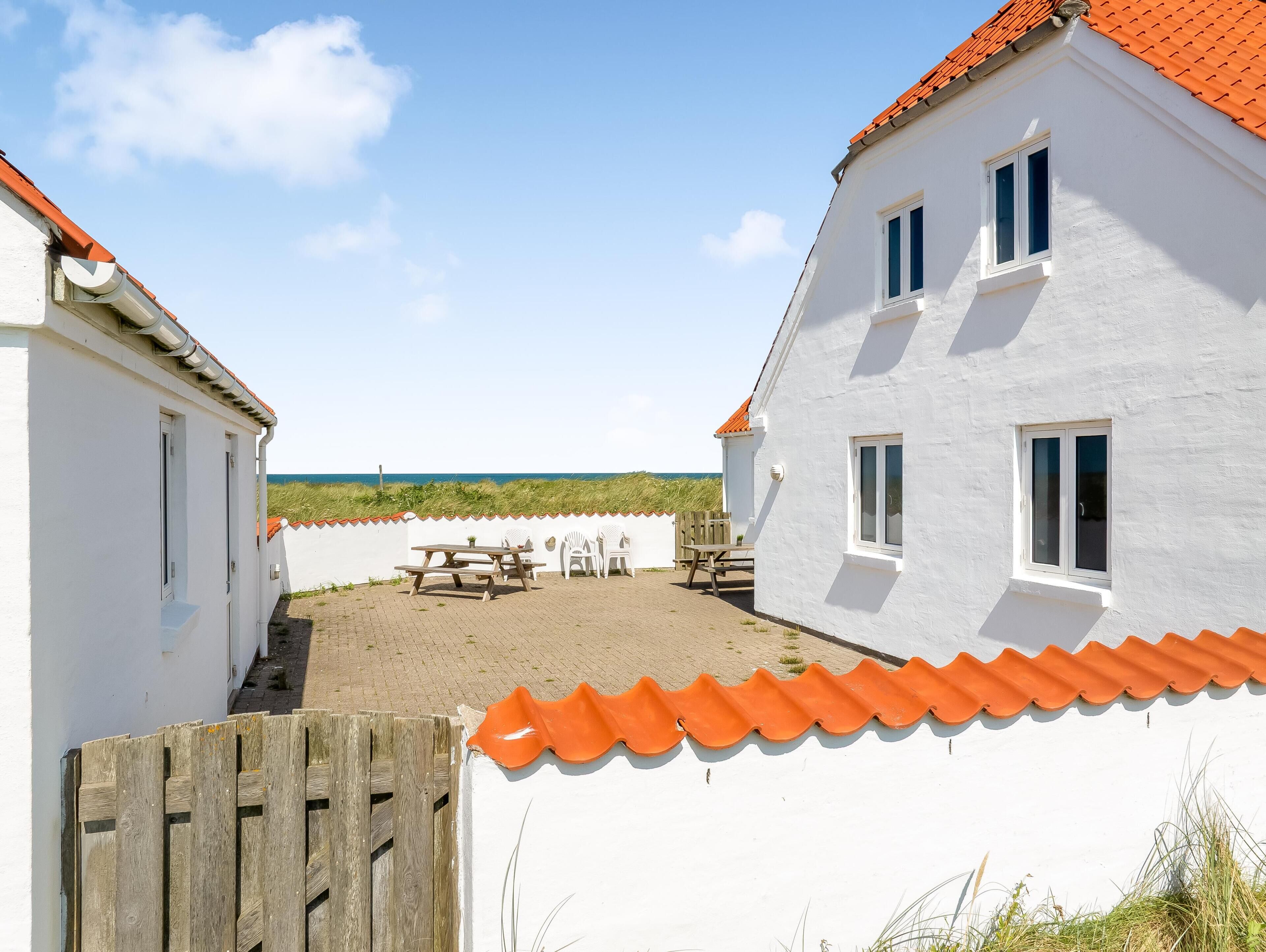 A white building with a red roof, a wooden fence, and a picnic table with chairs.