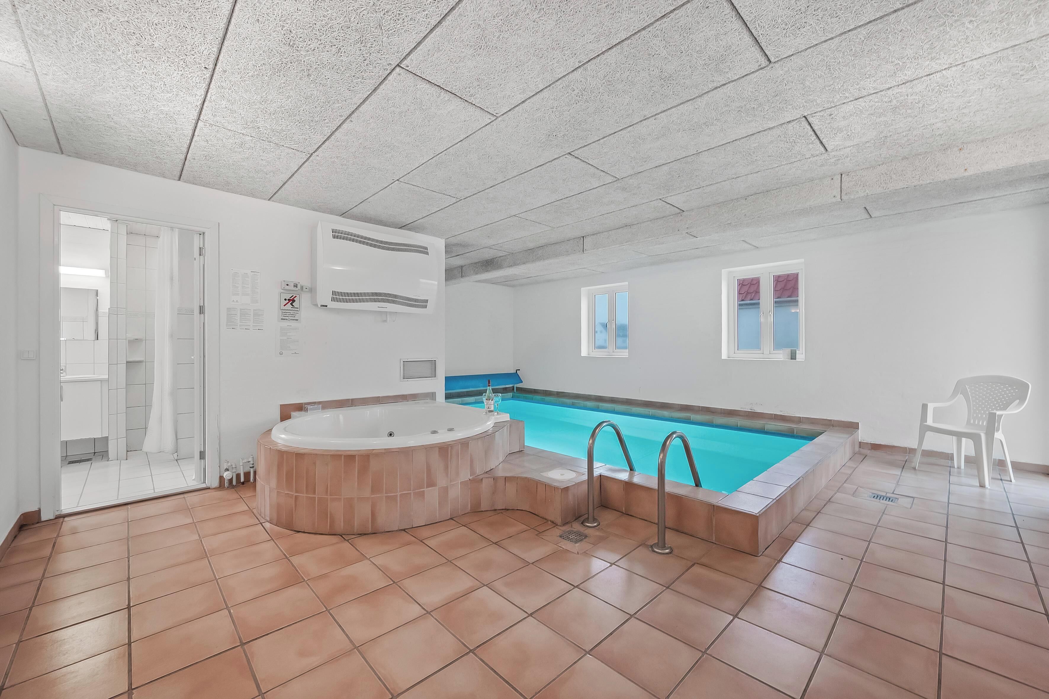 A spacious indoor swimming pool with a hot tub, a shower area, and a view of the outside.