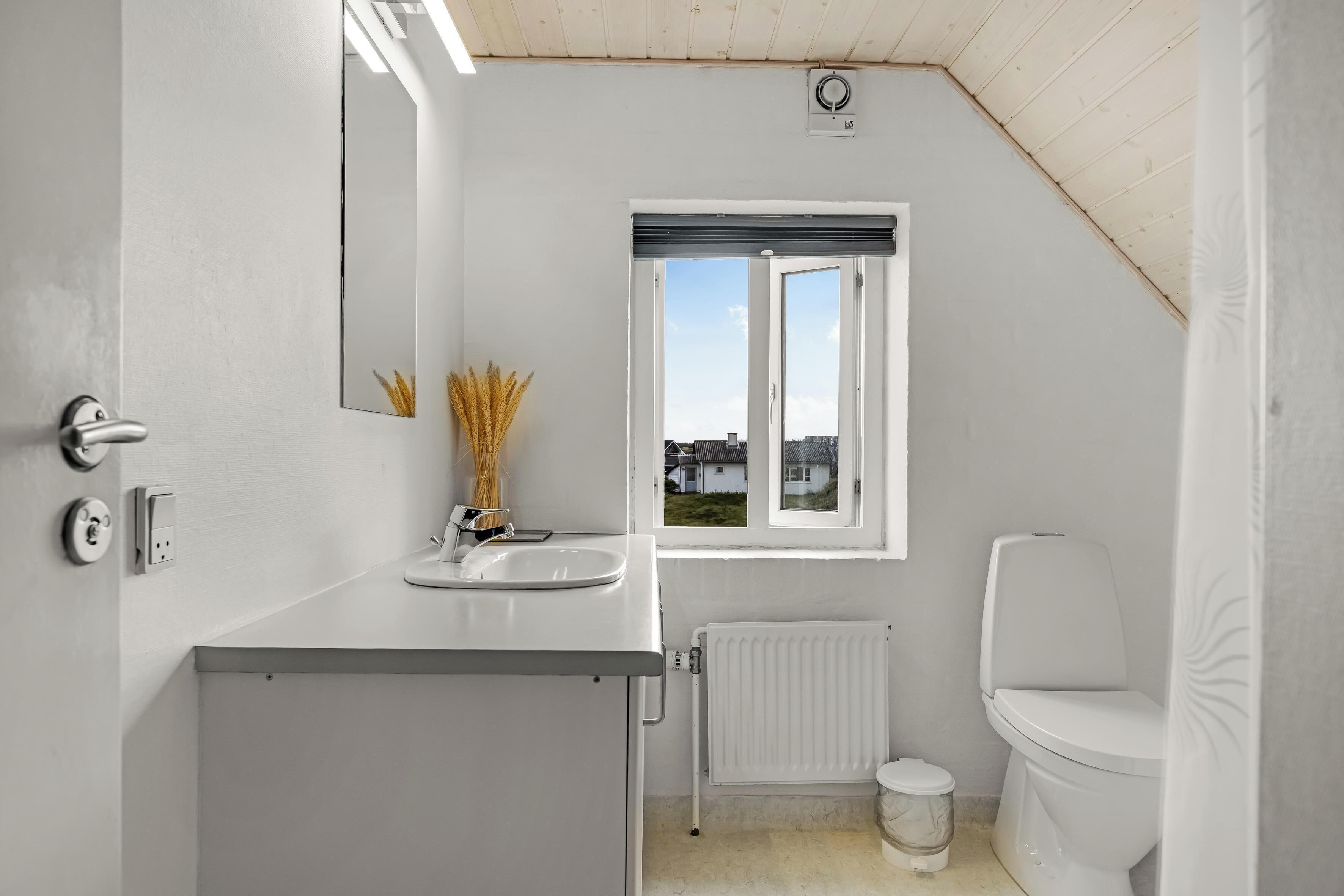 Une petite salle de bain blanche, avec une fenêtre, un radiateur et des toilettes.
