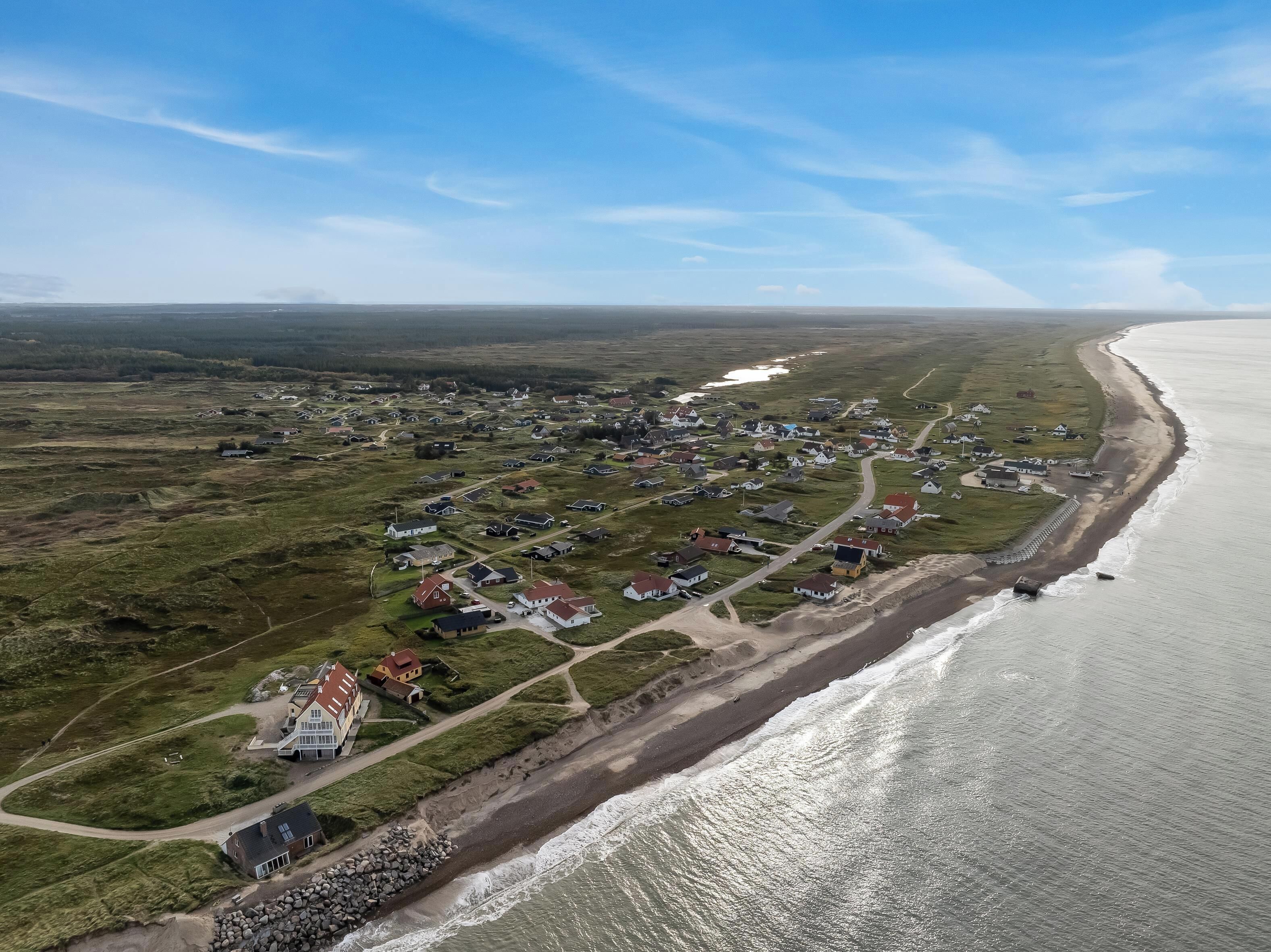 En vy från ovan över en kustby med hus längs strandlinjen, en strand och en klar himmel.