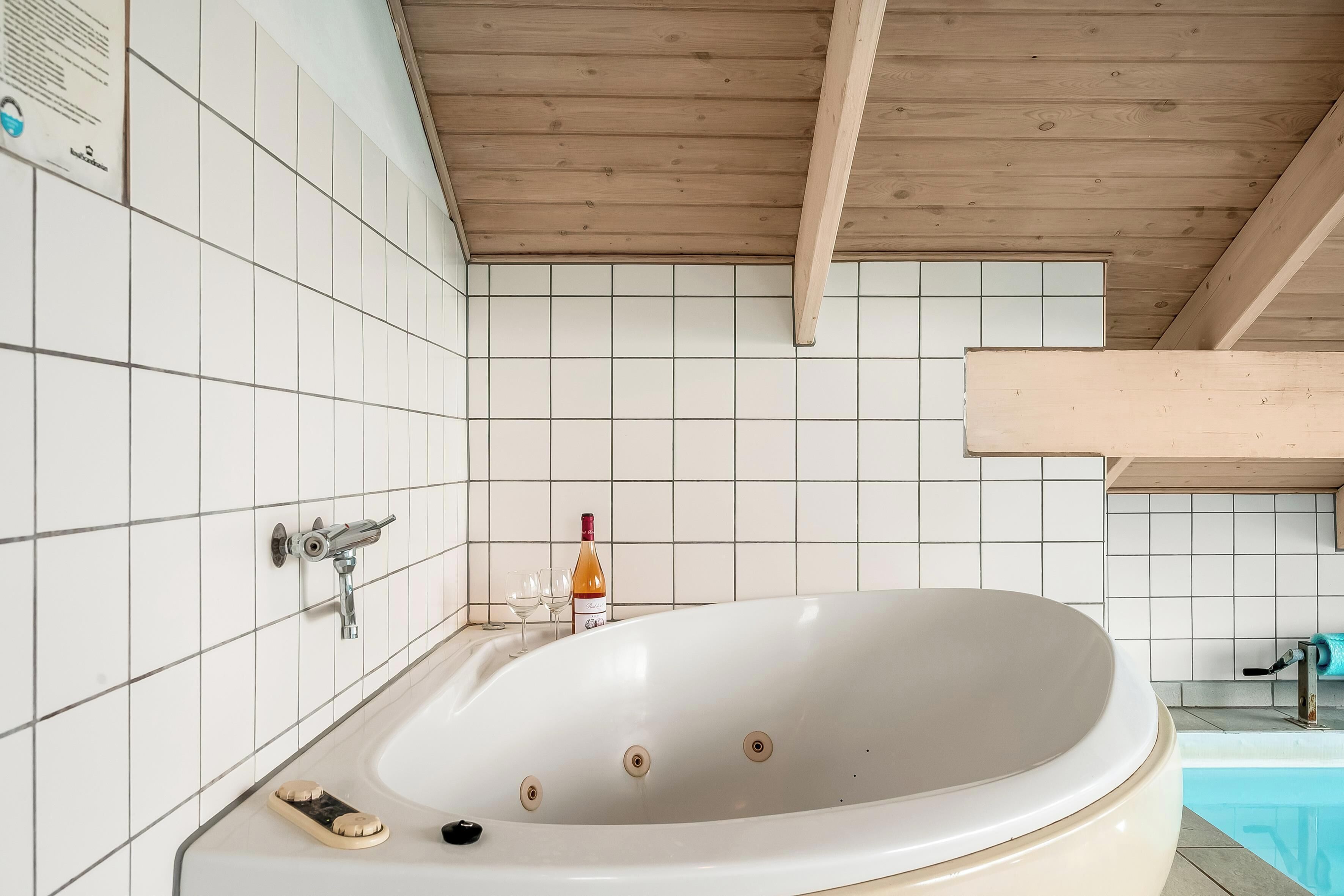 Un baño moderno con una bañera independiente, paredes cubiertas de azulejos blancos y techo de madera.