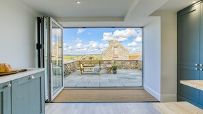 A modern kitchen with a large sliding glass door leading to a patio with a stone wall and a wooden bench. - Trecastell - sleeps 8 guests  in 4 bedrooms (Rhosneigr)