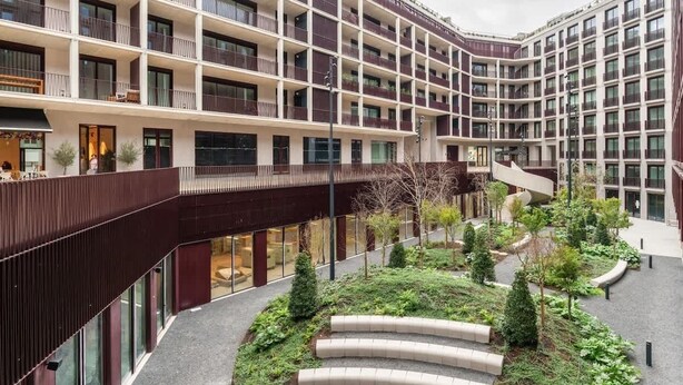 En byggnad med flera våningar, balkonger, en central innergård med grönska och en modern arkitektonisk design.