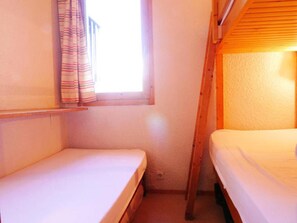 Una habitación pequeña y estrecha con dos camas individuales y una ventana con cortinas.