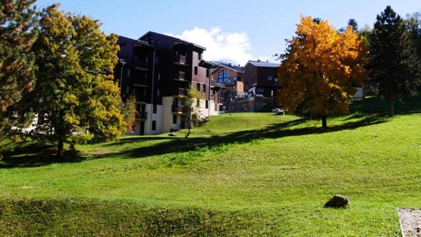 Zona residencial con edificios de varios pisos, una colina cubierta de pasto y árboles con follaje otoñal.
