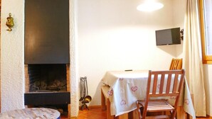 Una habitación acogedora con chimenea, una mesa de comedor con sillas, un televisor montado en la pared y una ventana con cortinas.