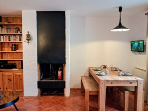 A cozy room with a fireplace, wooden shelves, a dining table set for two, and a television on the wall.