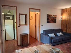 A living room with a blue sofa, a wooden cabinet, a dining table with wine glasses, and a painting on the wall.