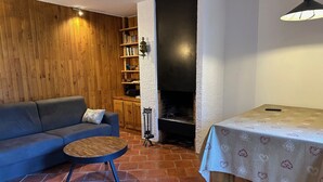 Un salón acogedor con un sofá azul, una mesita redonda, una estantería y una chimenea.