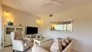 Un salon équipé d’un téléviseur, de deux canapés, d’une table basse et d’un ventilateur de plafond.