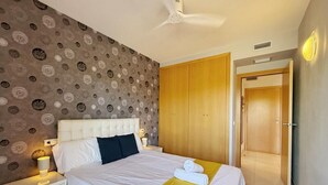 Une chambre d’hôtel avec un papier peint à motifs, un lit avec une literie blanche, une armoire en bois et un ventilateur de plafond.