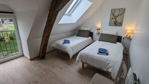 Une chambre avec deux lits, une lucarne, un tableau et une lampe.