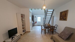 A living room with a TV, a sofa, a dining table with chairs, a white cabinet, and a staircase leading to another room. - Gîte 1 Les Ratys: charm, tranquility and comfort near Orleans (Chaingy)
