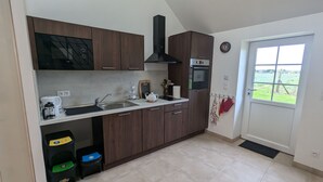 A modern kitchen with wooden cabinets, a built-in oven, a coffee maker, and a window with a view of the countryside. - Gîte 1 Les Ratys: charm, tranquility and comfort near Orleans (Chaingy)