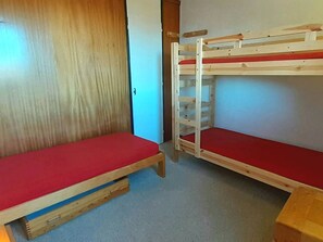 A bunk bed with a red mattress in a room with a wooden door and a white wall.