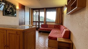 Une pièce chaleureuse avec un banc en bois, une petite table et une vue sur l’extérieur grâce à de grandes fenêtres.