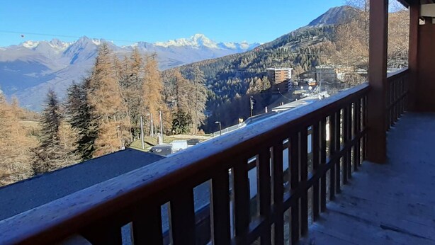 Un balcon offrant une vue sur un paysage montagneux, avec des pics enneigés et une vallée boisée.