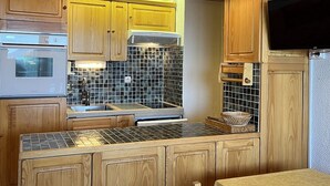 Une cuisine compacte avec des meubles en bois, un pare-feu en carrelage et des appareils électroménagers intégrés.