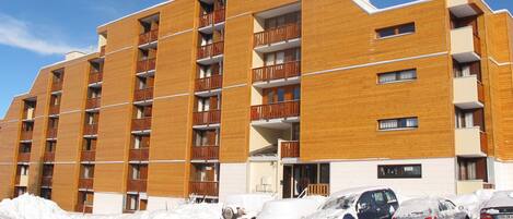A multi-story hotel with a wooden facade, balconies, and a parking area covered in snow.