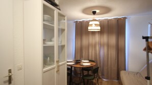 A compact room with a dining table set for two, a single chair, a sofa, and a cabinet with glass doors.
