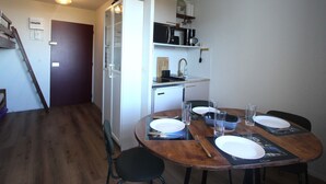 A compact kitchen with a refrigerator, microwave, and coffee maker. A dining table with chairs is set for four.
