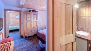Una stanza in legno con un letto, un armadio, una sedia e una porta che dà su un bagno.