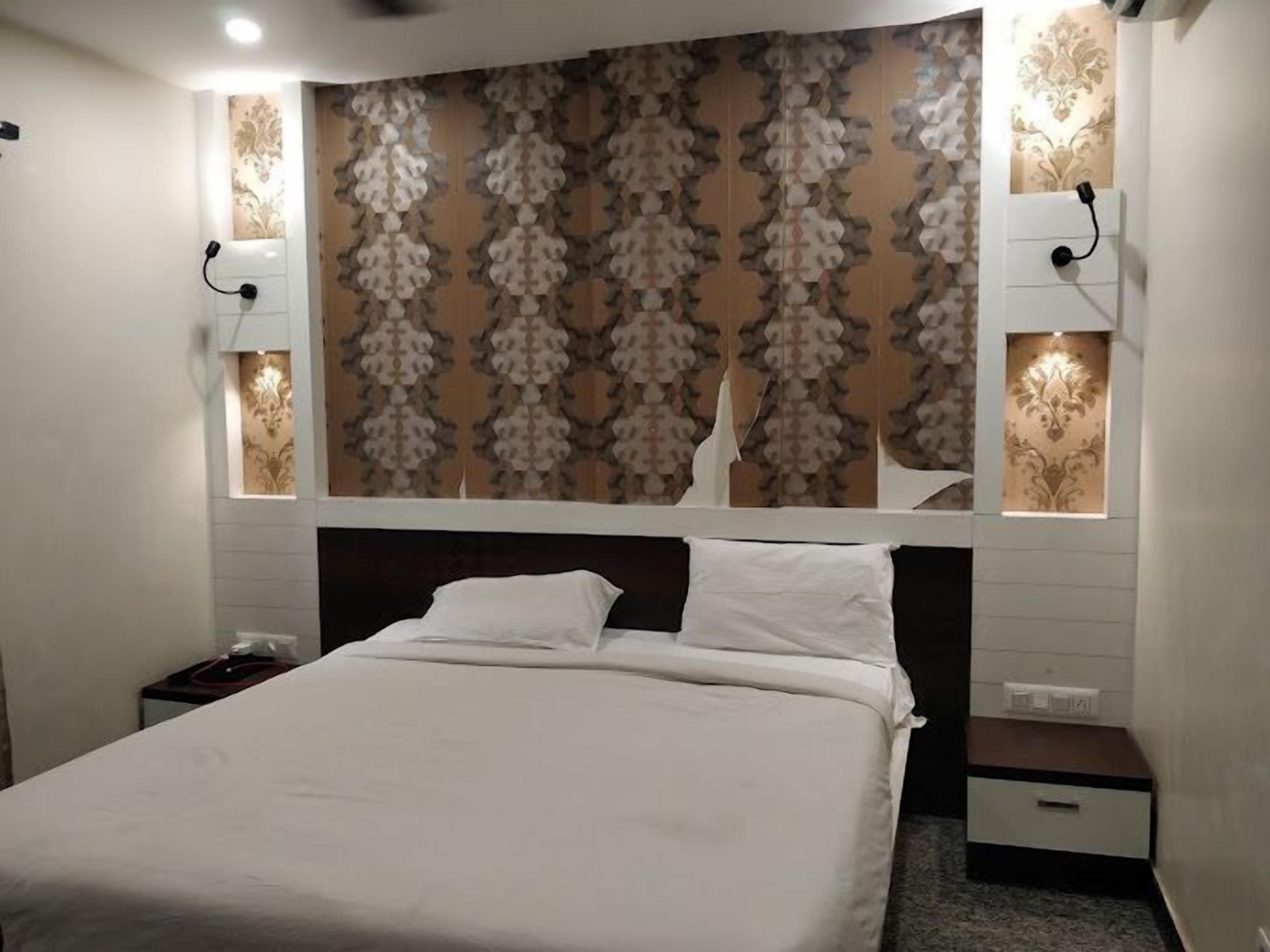 Een netjes opgemaakt bed in een hotelkamer, met een behangetjes hoofdbord, nachtlampjes en een klein nachtkastje.
