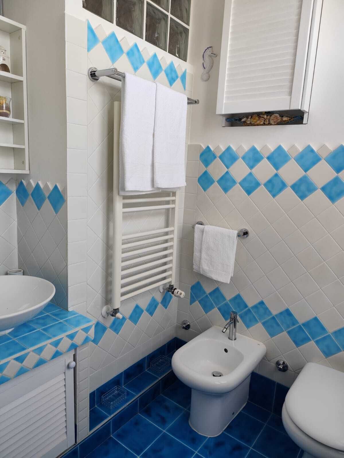 A bathroom with a white sink, a bidet, and a toilet. The walls have a blue and white diamond pattern.