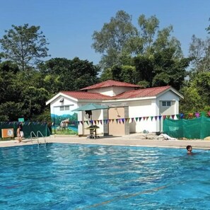 Una piscina con una casa al fondo, rodeada de árboles.