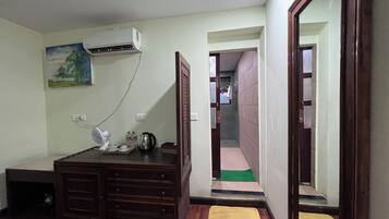 Habitación de hotel con cómoda de madera, equipo de aire acondicionado, ventilador, un cuadro y baño visible a través de una puerta abierta.