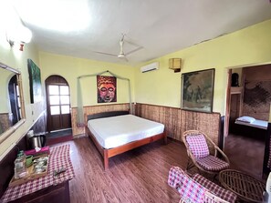 Una habitación con una cama, una silla, una mesa con objetos, un ventilador de techo y obras de arte en las paredes.