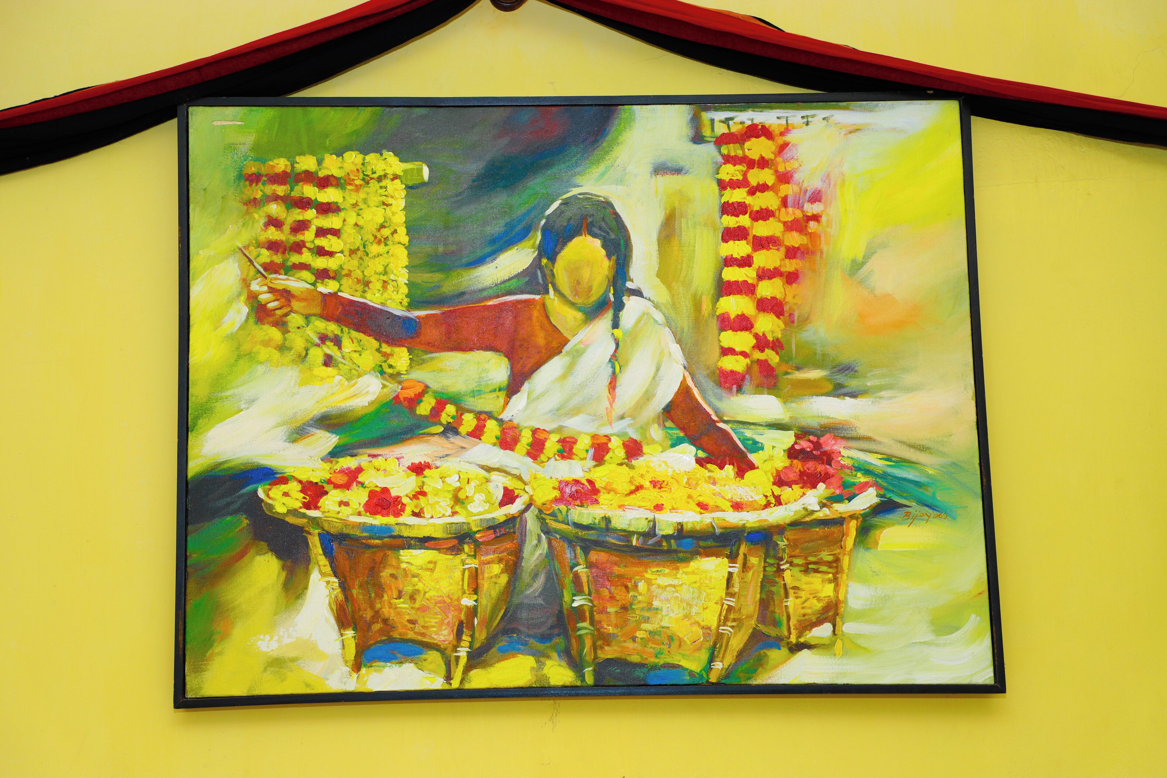 A painting of a woman playing a drum, surrounded by flowers and draped in a white sari, against a yellow wall.