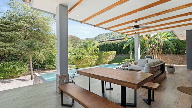 Une terrasse extérieure moderne, dotée d’une table en bois, de bancs et d’une piscine.