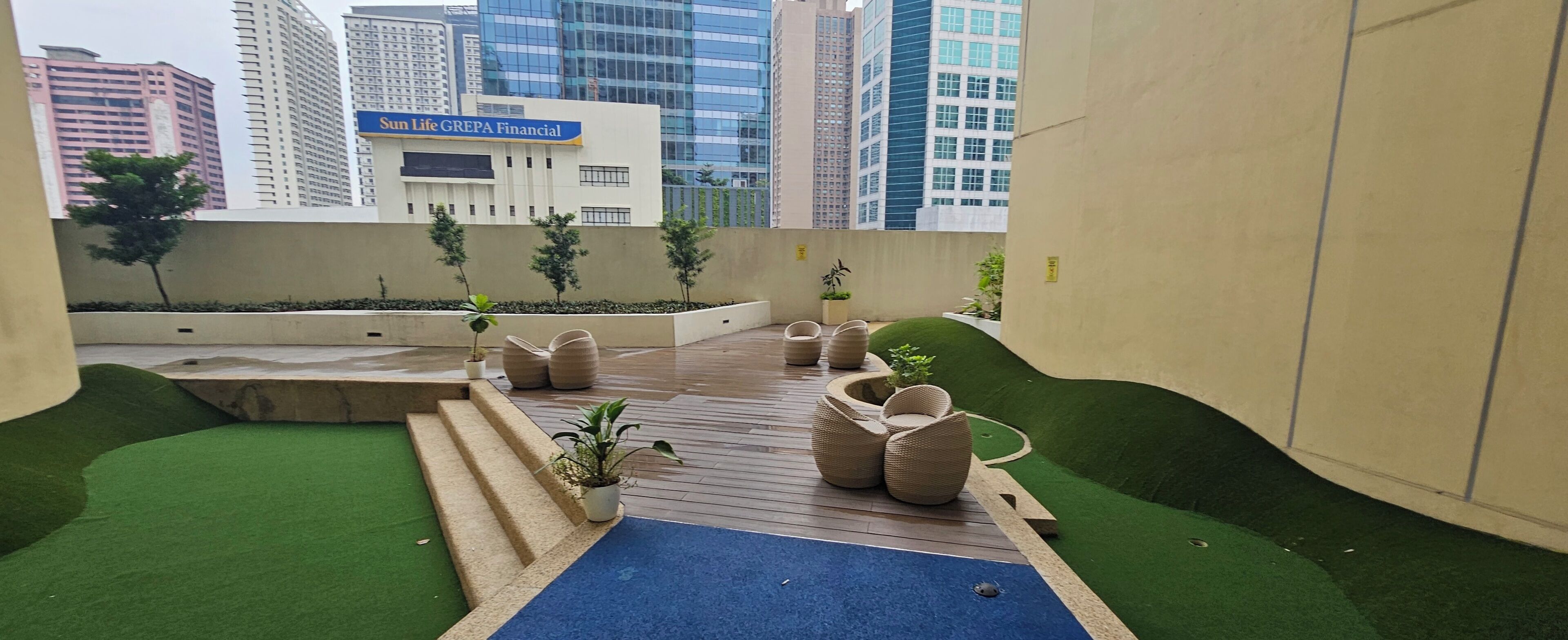 A rooftop garden with seating areas, potted plants, and a view of the cityscape including a building with a sign reading "Sun Life GREPA Financial".