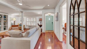 A spacious living room with a sectional sofa, a wooden coffee table, and a bookshelf. A hallway leads to a door with a unique design.