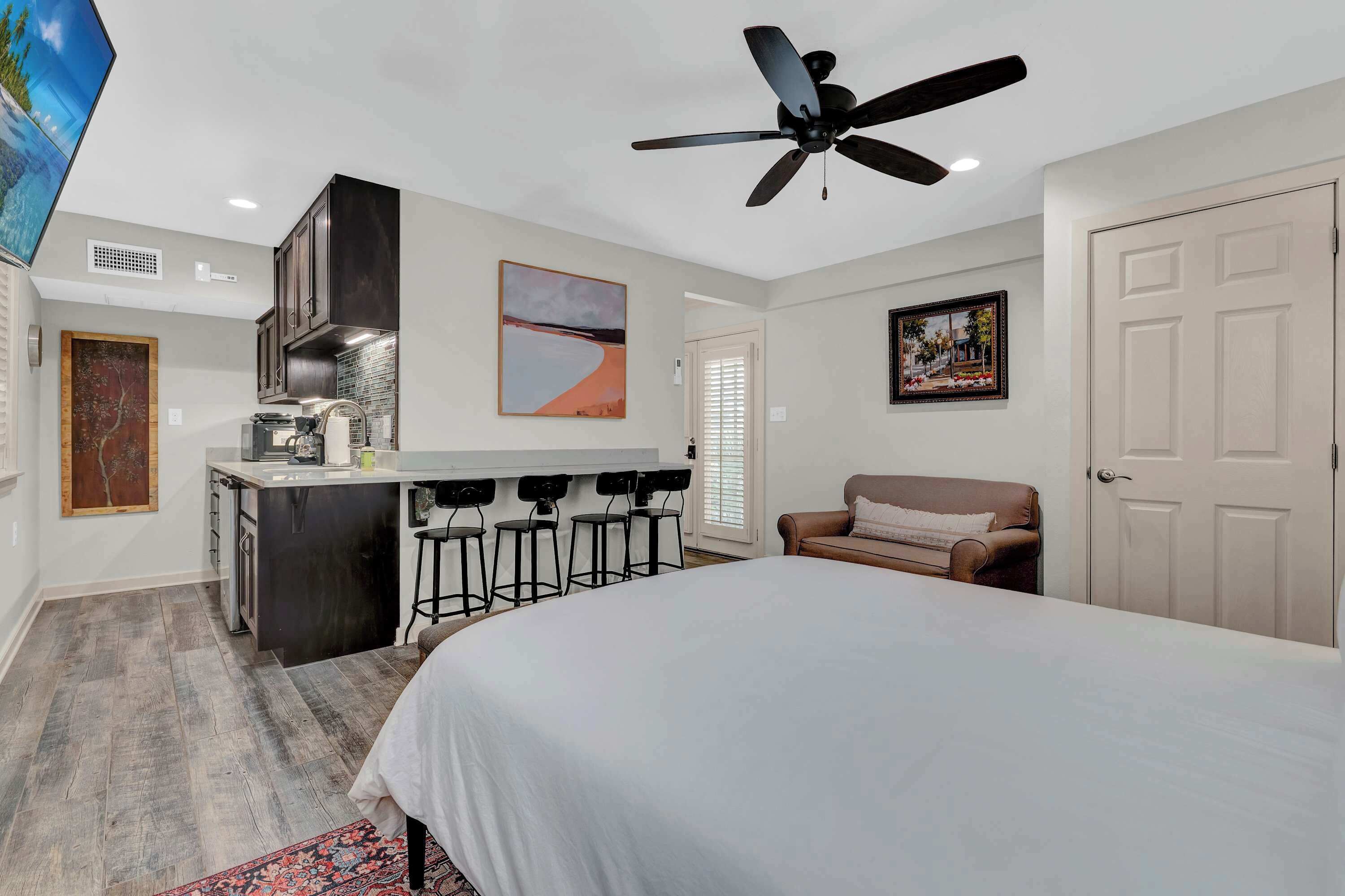 Une chambre d’hôtel moderne dotée d’un grand lit, d’une kitchenette, d’un ventilateur de plafond et d’une télévision.