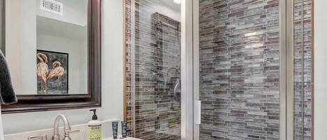 A modern bathroom with a glass shower enclosure, a vanity with a sink, and a mirror with a framed artwork.