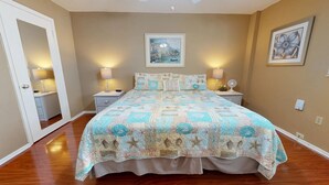 Une chambre avec un grand lit, deux tables de chevet avec des lampes, une porte donnant sur une salle de bain et un tableau accroché au mur.