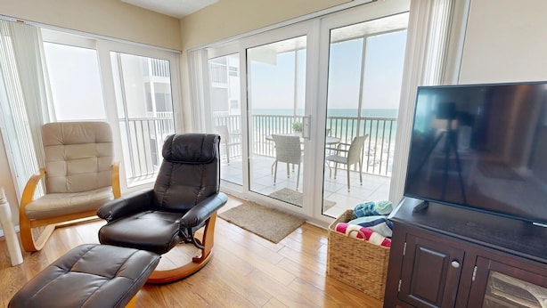 Un balcon spacieux avec un fauteuil en cuir, un fauteuil en osier et un téléviseur.