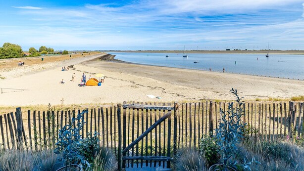 A beach with a wooden fence, sandy shore, and calm water. - Apartment in Sint-annaland With Beach Access (Sint-Annaland)
