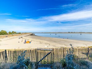 A beach with a wooden fence, sandy shore, and calm water. - Apartment in Sint-annaland With Beach Access (Sint-Annaland)