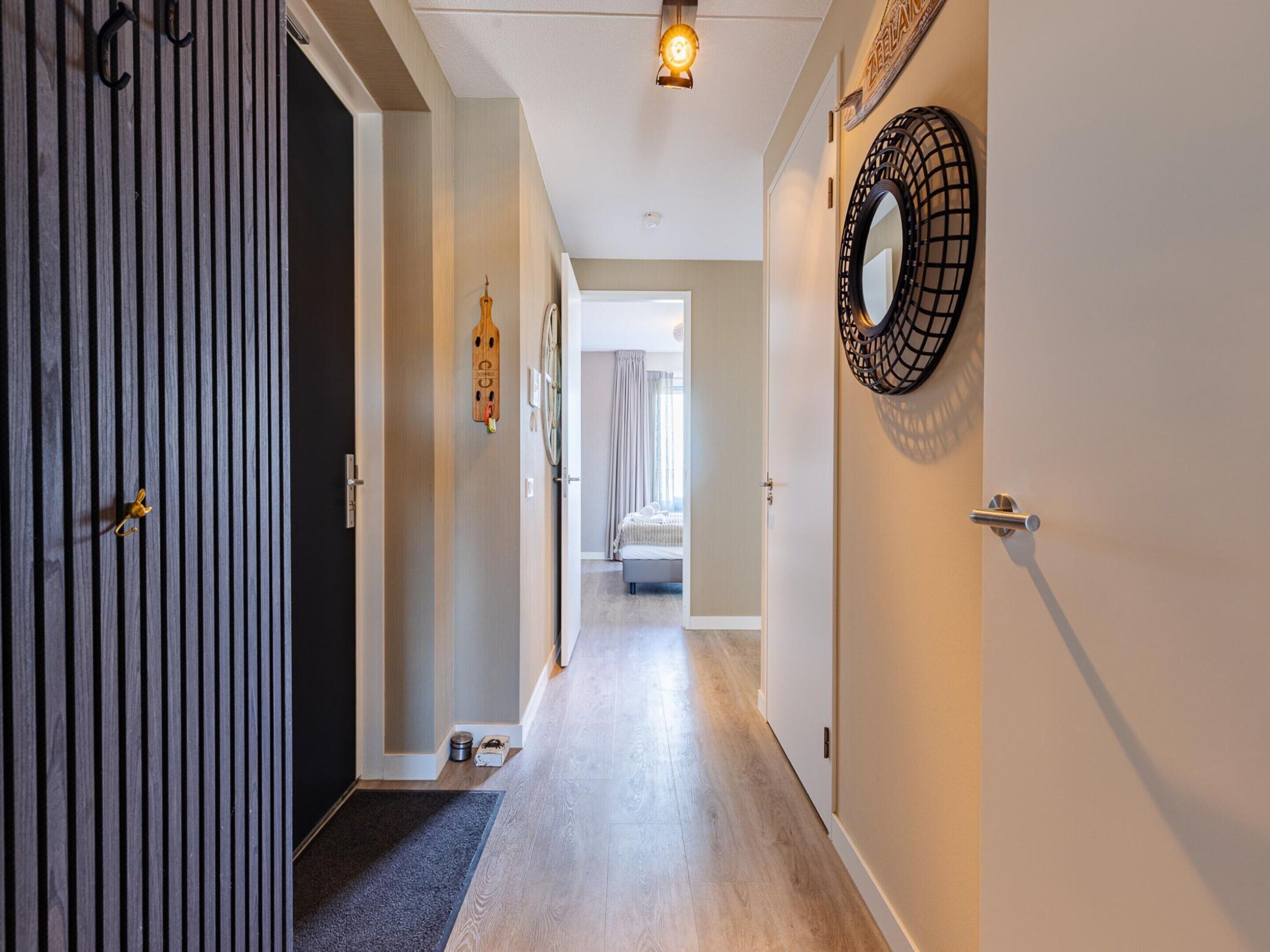 A hallway with a wooden door, a round mirror, and a bed in the background.