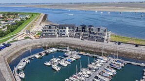 A marina with multiple boats docked, a large building with a modern design, and a clear view of the water and distant wind turbines. - Apartment in Sint-annaland With Beach Access (Sint-Annaland)