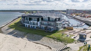 A modern building with multiple floors, a marina with boats, and a beach area. - Apartment in Sint-annaland With Beach Access (Sint-Annaland)