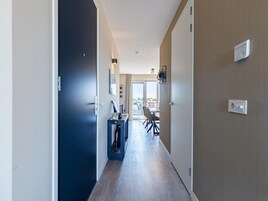 Un pasillo con una puerta oscura, una consola azul y un comedor con sillas y una mesa.