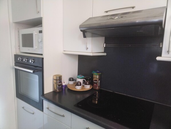 A compact kitchen with a microwave, oven, and black stove top. There are cabinets and a countertop with a few items like a coffee maker and a can of coffee.